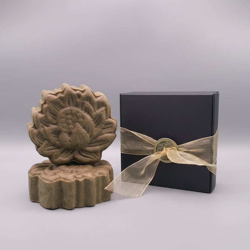 Green shampoo bar with a black box and gold ribbon on a gray background